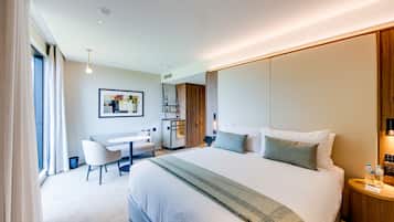 A modern hotel room with a large bed, a desk, and a chair. There is a small table with water bottles on it.