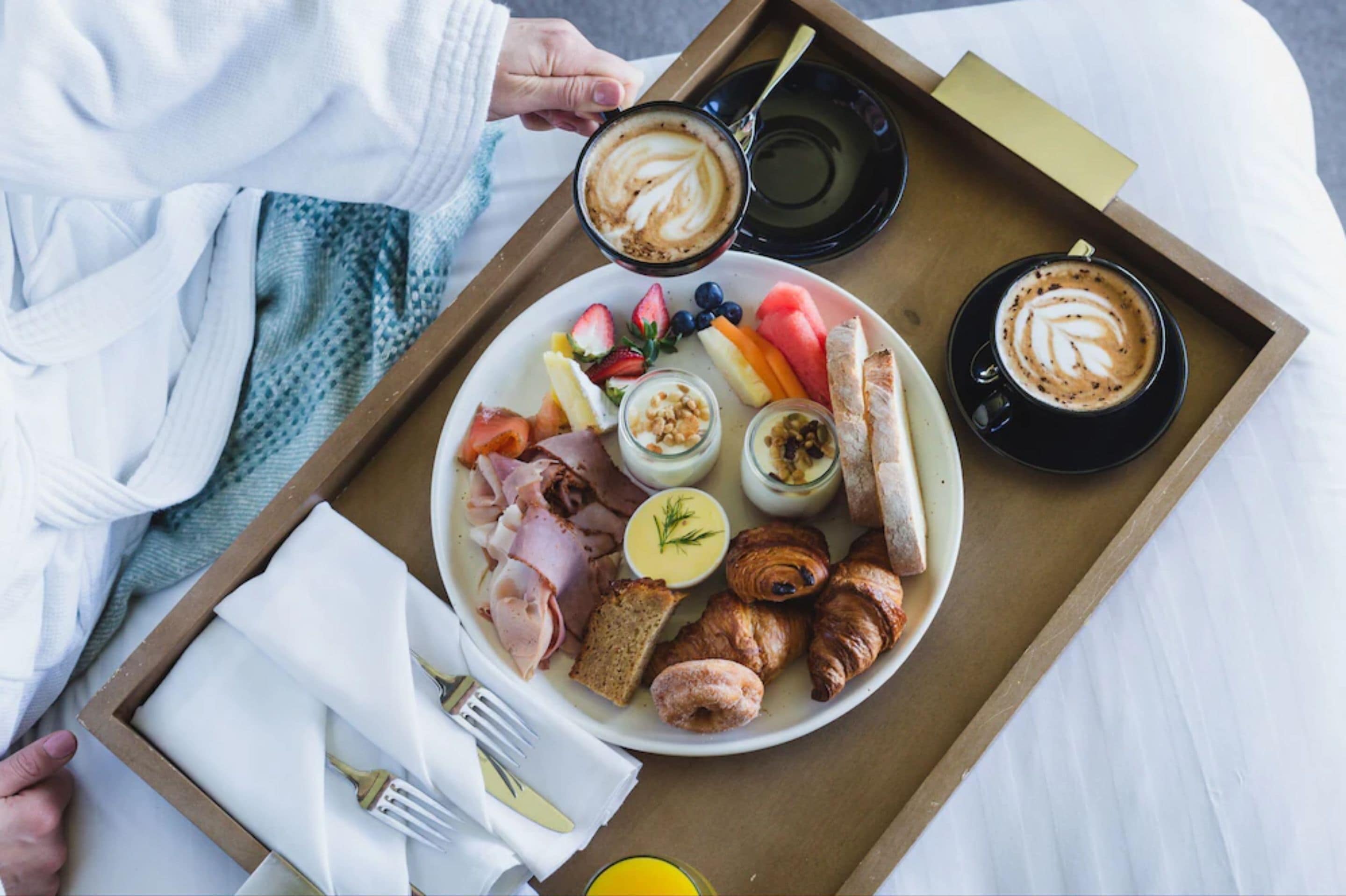 A breakfast tray with croissants, ham, eggs, fruits, and coffee.