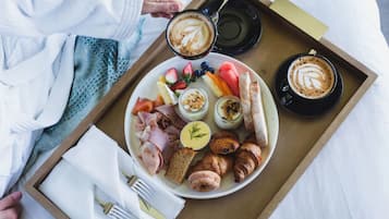 A breakfast tray with croissants, ham, eggs, fruits, and coffee.