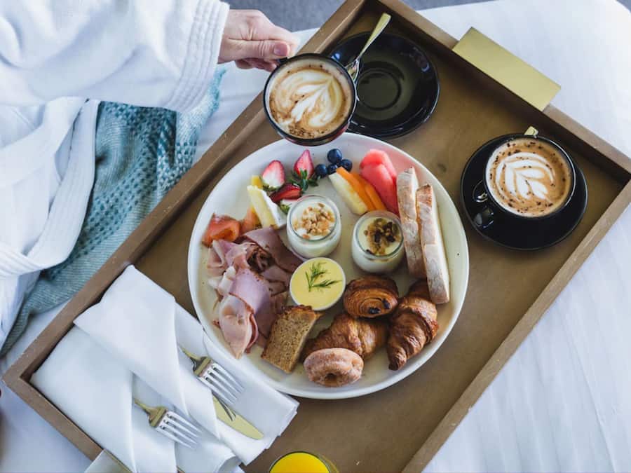 A breakfast tray with croissants, ham, eggs, fruits, and coffee.