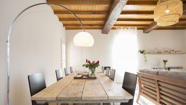A dining area with a wooden table, black chairs, a vase of red flowers, and a hanging light fixture.