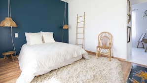 A bedroom with a bed, a white rug, a wooden ladder, and a wicker chair.