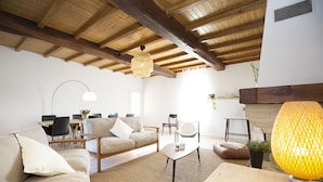 A spacious living room with a high wooden ceiling, a sofa set, a coffee table, and a floor lamp.