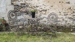 A rustic outdoor seating area with wrought iron chairs and a table, set against a stone wall backdrop.