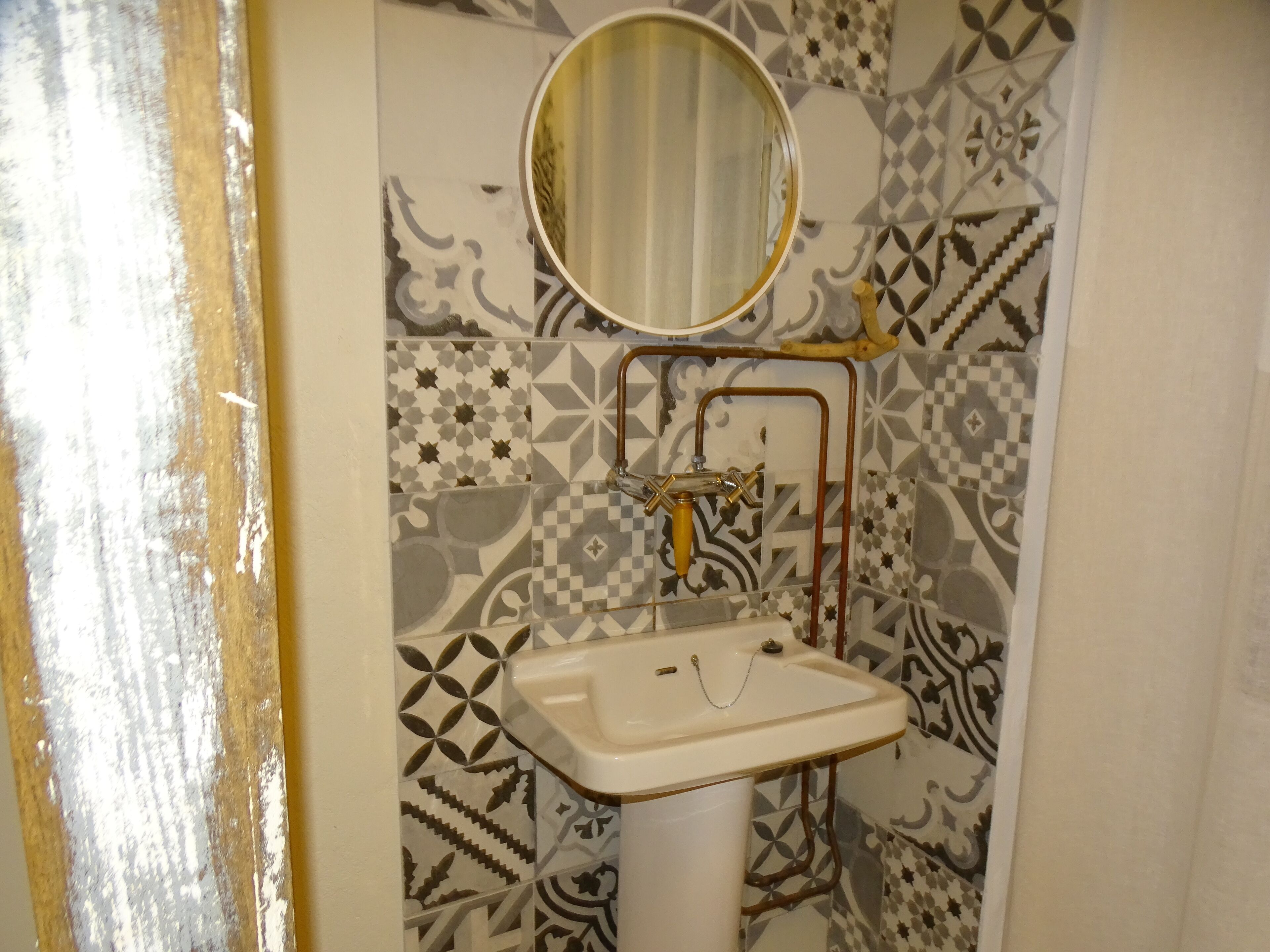 A bathroom with a white sink, a mirror, and a patterned tile wall.