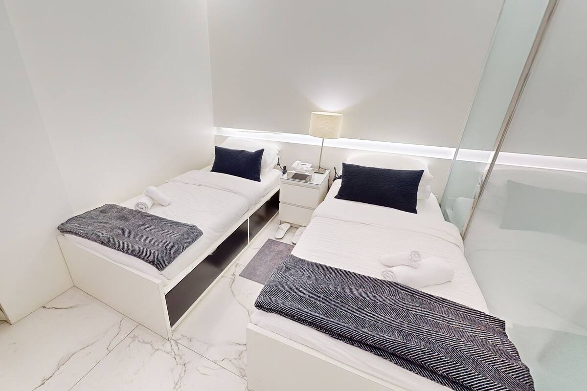 Habitación de hotel con dos camas, una mesita de noche, una lámpara y un espejo.