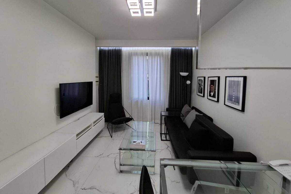 Una sala de estar moderna con una televisión de pantalla plana, una mesa de centro de vidrio, un sofá negro y una mesa de comedor de vidrio.