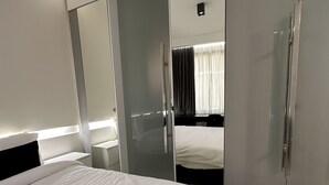 Une chambre d’hôtel moderne dotée d’un grand lit, d’un dressing et d’une salle de bain avec une douche en verre.