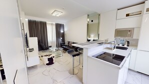 Une chambre d’hôtel moderne dotée d’une kitchenette, d’un coin salon avec un canapé et des fauteuils, et d’un grand miroir.