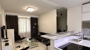 Une cuisine moderne avec un plan de travail blanc, une cuisinière encastrée et un évier. On y trouve un coin repas avec une chaise noire et une table en verre. La pièce est dotée de murs blancs et d’un sol en marbre.
