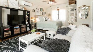 A cozy bedroom with a bed, a TV, a bookshelf, and a ceiling fan.