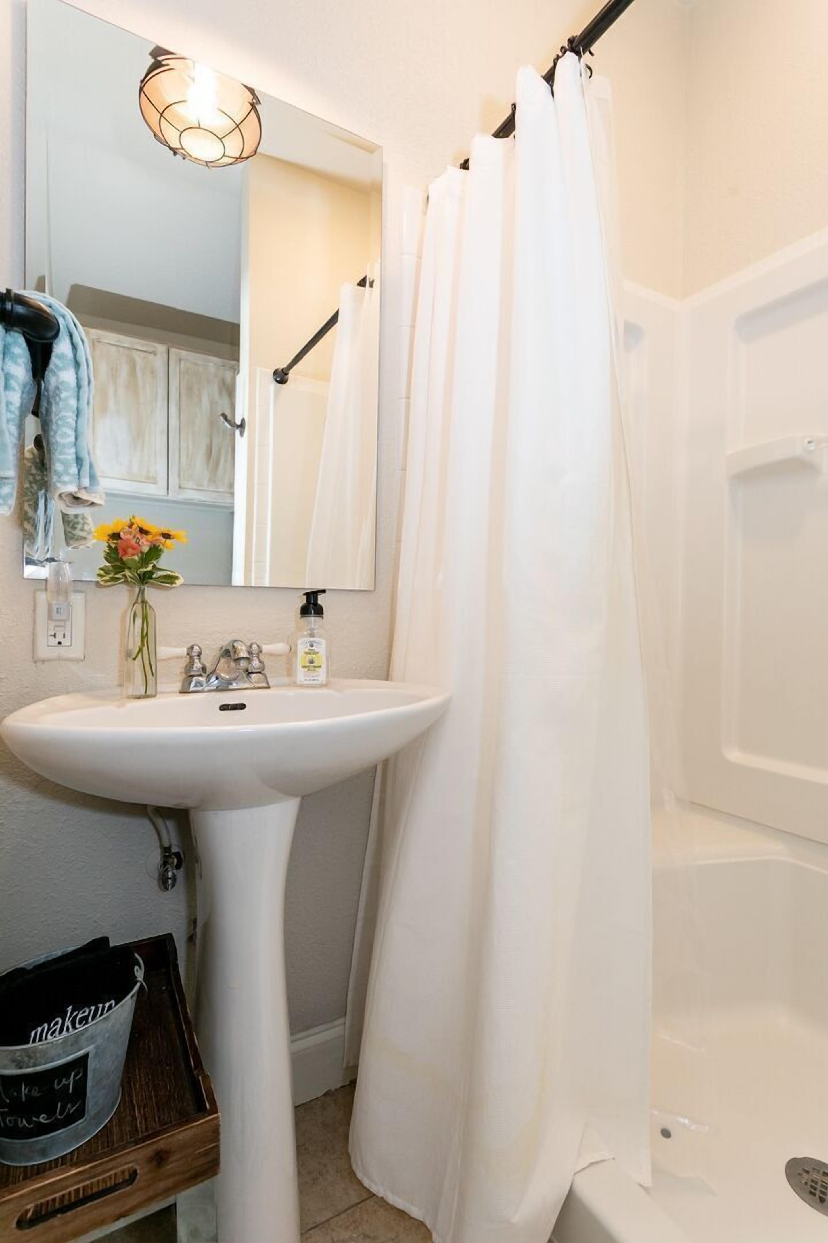 A bathroom with a white sink, a mirror, a shower curtain, and a small wooden tray with a bucket labeled "makeup".