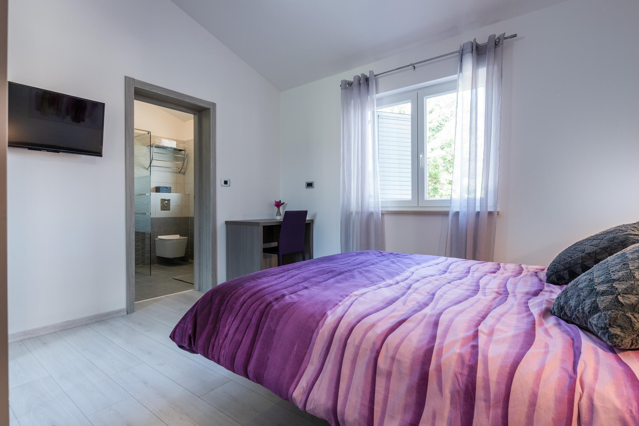Een slaapkamer met een bed, een televisie, een bureau, en een badkamer zichtbaar door een geopende deur.
