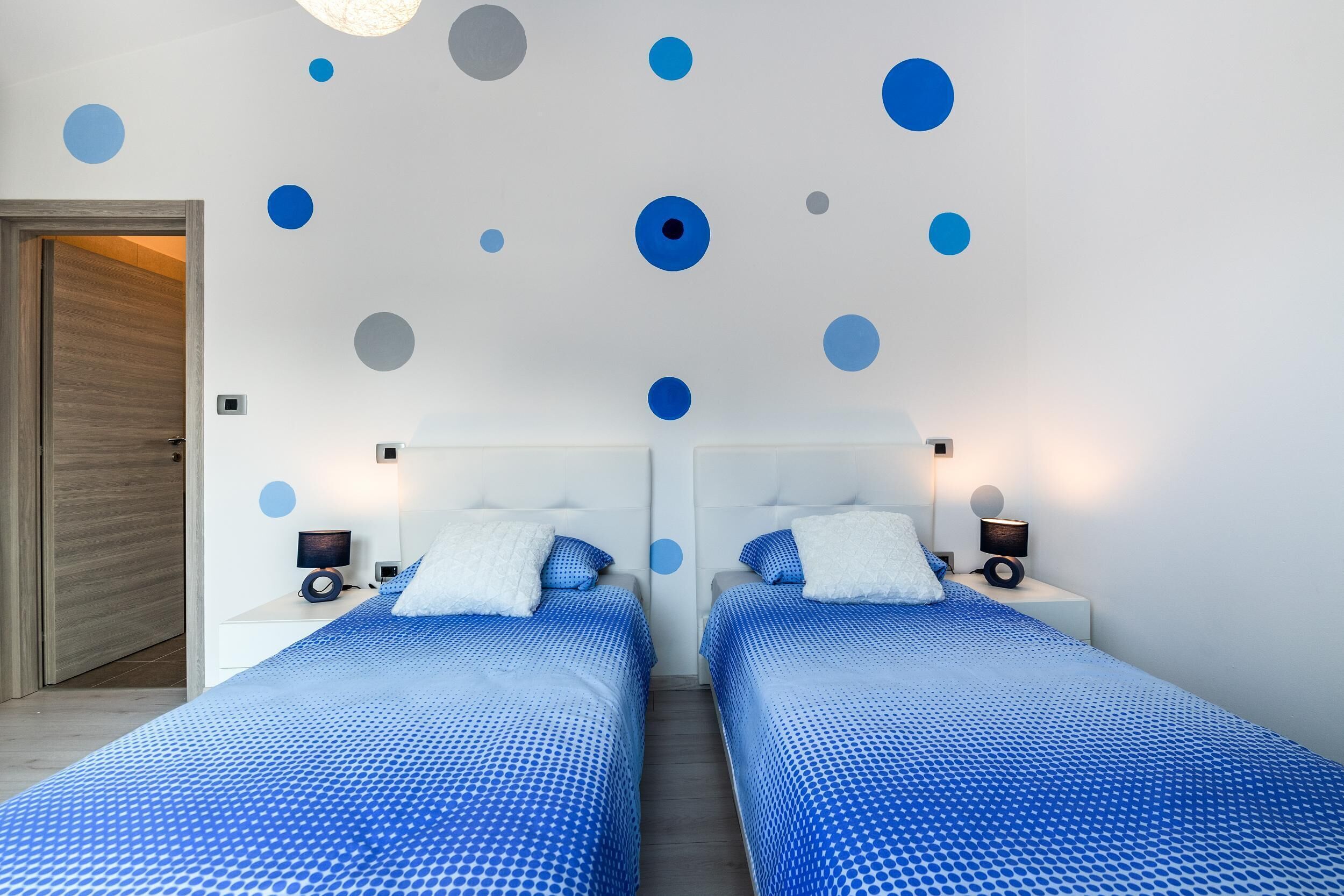 Une chambre moderne avec deux lits, une porte en bois et un mur décoré de cercles bleus et gris.