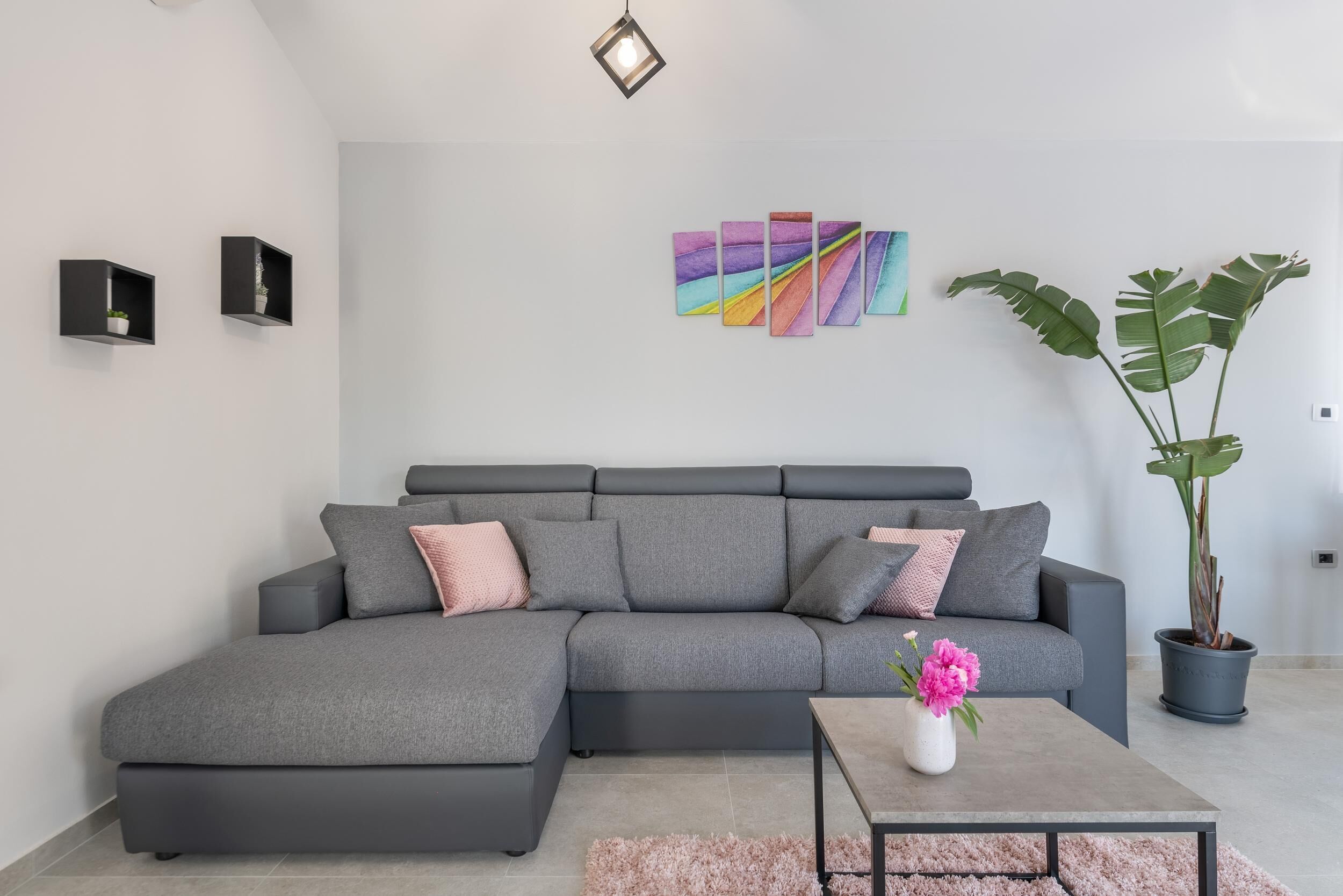 Una sala de estar moderna con un sofá seccional gris, una mesa de centro, una planta en maceta y un cuadro abstracto colorido en la pared.
