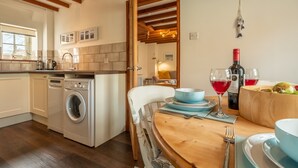 Een keuken met een wasmachine, houten balken, een eettafel gedekt met borden, kommen en wijnglazen.