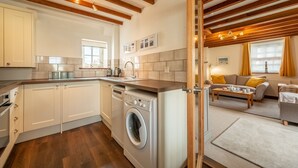 Een moderne keuken met een ingebouwde wasmachine en droger, houten balken en een gezellig woongedeelte met een bank en salontafel.