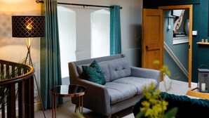 A living room with a grey sofa, a small round table, a floor lamp, and a staircase leading to an upper level. - Canon Gate , Chichester Cathedral  - sleeps 4 guests  in 2 bedrooms (Chichester)