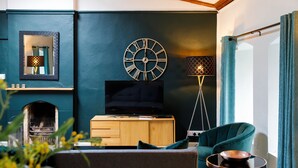 A modern living room with a TV, wooden cabinet, teal armchair, and a floor lamp. - Canon Gate , Chichester Cathedral  - sleeps 4 guests  in 2 bedrooms (Chichester)