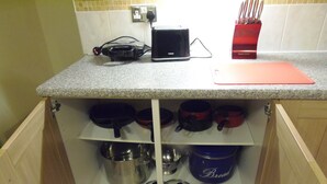 A kitchen with a countertop, a toaster, a red knife holder, and various pots and pans on shelves. - Light and Airy 1 bed Flat With Large Basement Kitchen and Private Outside Area (leeds)