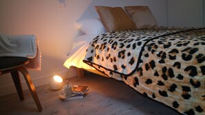 Un dormitorio con una cama cubierta por una manta de estampado de leopardo, una mesita de noche con una lámpara y una silla con una manta.