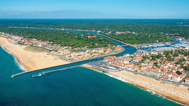Vista aérea de un pueblo costero con puerto deportivo, playa y zonas residenciales.
