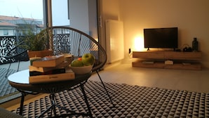 Una sala de estar moderna con una silla negra, una mesa de vidrio, un cuenco de manzanas, un televisor y una alfombra estampada.
