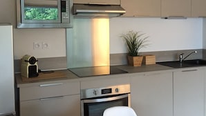 Una cocina moderna con microondas, horno y estufa a gas. Hay una mesa de comedor con sillas y una planta en maceta.