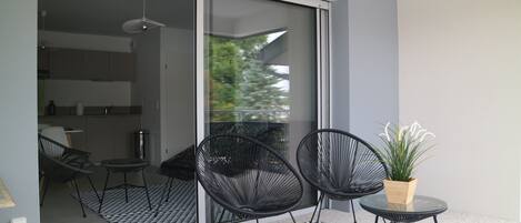 A modern balcony with two black chairs, a small table, and a potted plant.