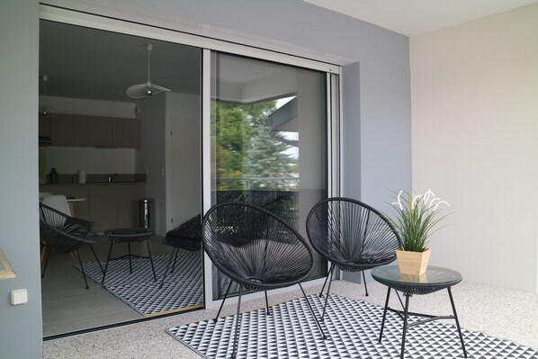 A modern balcony with two black chairs, a small table, and a potted plant.