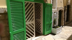 Um pátio com piso de pedra, uma porta branca e contraportas verdes.