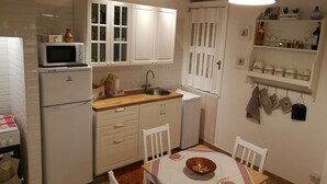 Uma cozinha compacta com armários brancos, micro-ondas, pia e um espaço de jantar com mesa posta para dois.