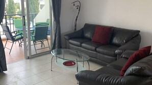 A living room with a leather sofa, a glass coffee table, and a dining area with green chairs and a table. - KINGS SUNSET, PAPHOS (Paphos)