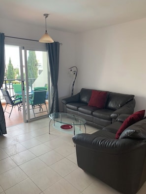 A living room with a leather sofa, a glass coffee table, and a dining area with green chairs and a table. - KINGS SUNSET, PAPHOS (Paphos)