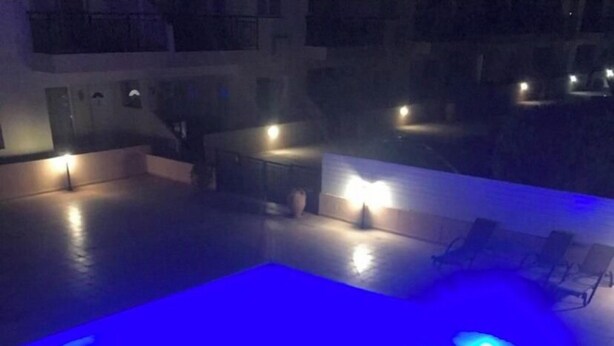 A swimming pool with blue lighting, surrounded by lounge chairs and a building in the background. - KINGS SUNSET, PAPHOS (Paphos)