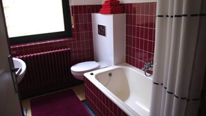 Ein Badezimmer mit einer weißen Badewanne, einer weißen Toilette und einer roten Fliesenwand.