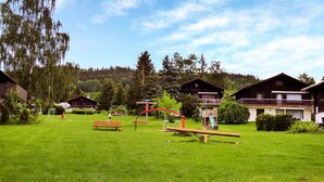 Eine begrünte Außenanlage mit Spielgeräten, Bänken und Holzhütten.