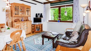 Ein gemütliches Wohnzimmer mit einem Holzschrank, einem Fernseher, einer Ledersofa und einem Essbereich mit Tisch und Stühlen.