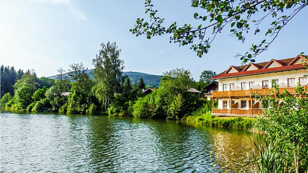 Ein Hotel am Seeufer mit Balkon, umgeben von üppigem Grün und einer stillen Seelandschaft.