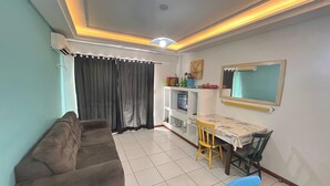 A living room with a sofa, a dining table with chairs, a TV, and a ceiling light fixture. - 222, apartment in a gated community with a shared swimming pool. (Bombas)