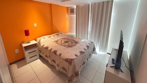 A bedroom with a large bed, a nightstand, a TV, and a window with curtains. - 222, apartment in a gated community with a shared swimming pool. (Bombas)