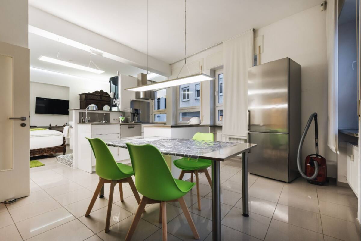 Una cocina moderna con una mesa de comedor, sillas verdes, un refrigerador y un aspirador.