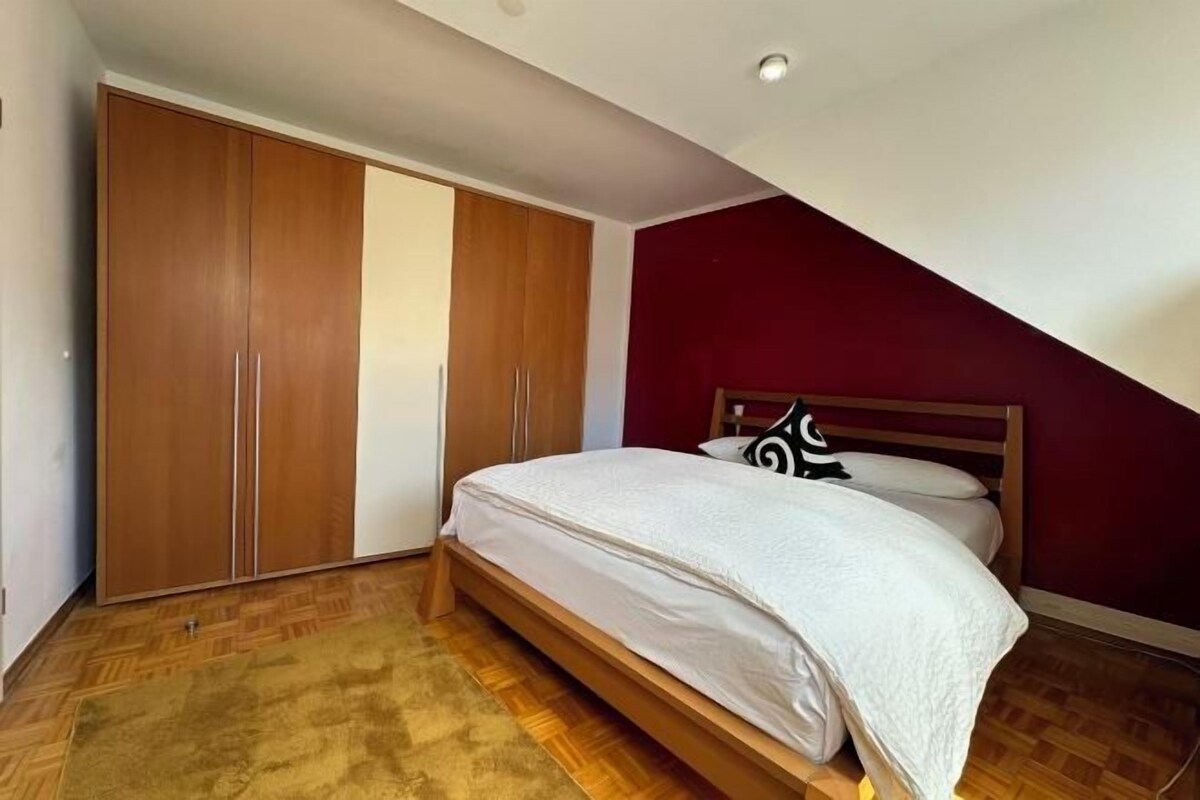 A bedroom with a bed, wooden wardrobe, and a sloped ceiling.