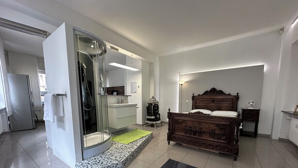 Une chambre à coucher comprenant un lit, un dressing, une salle de bain avec une douche en verre et un sol carrelé.