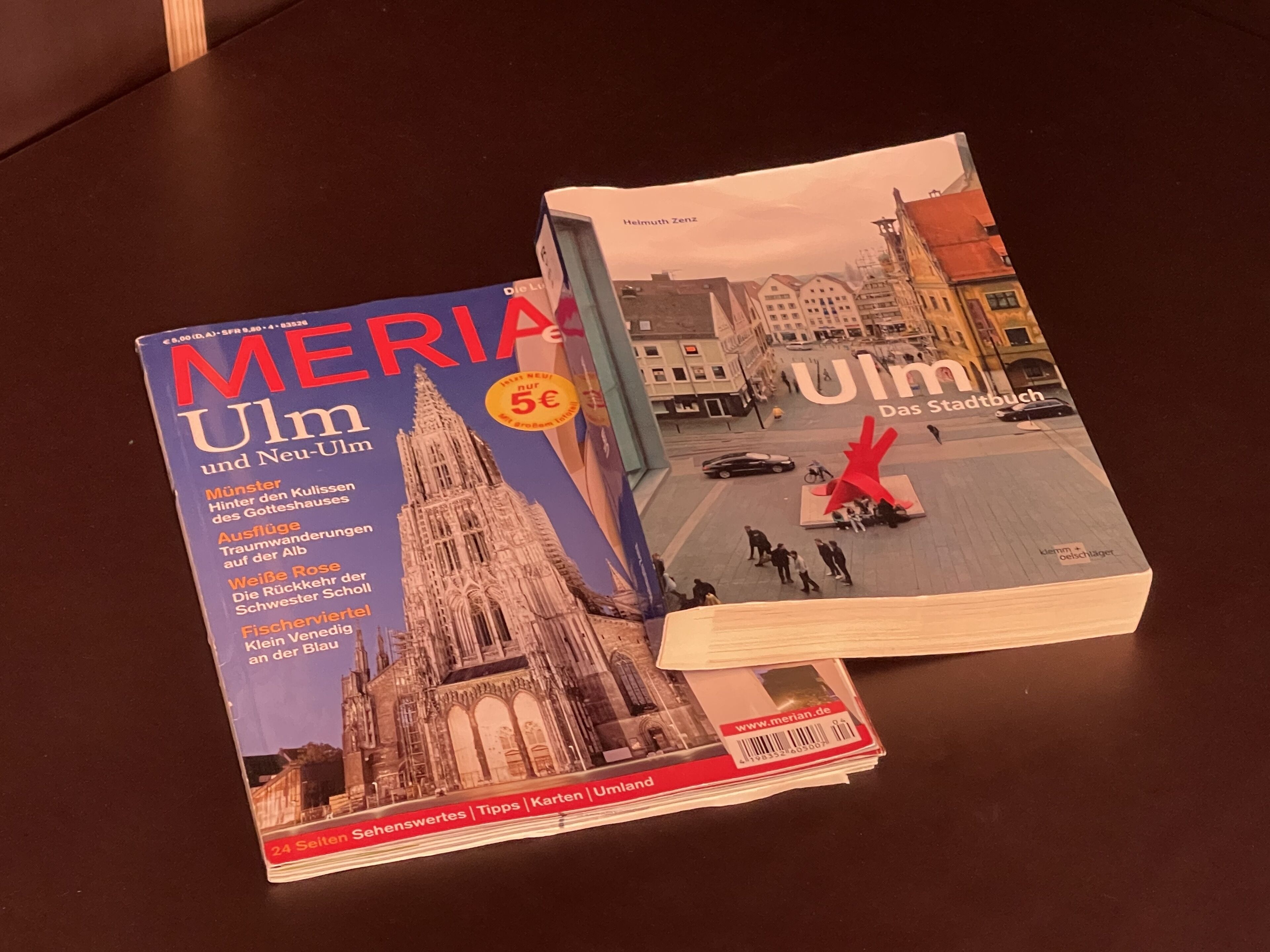 Un libro titulado 'MERIA Ulm und Neu-Ulm' con una portada que muestra una catedral y una escultura roja.