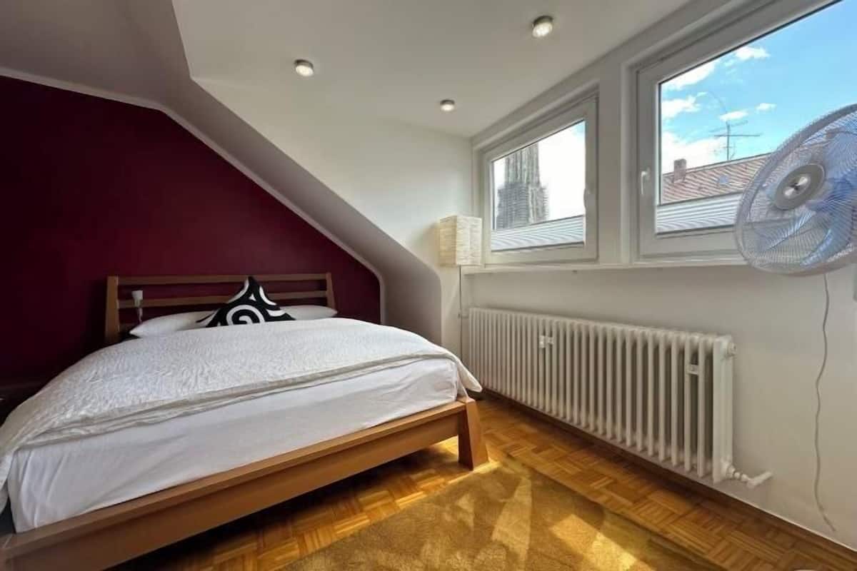Un dormitorio con cama, radiador, ventana con persianas y ventilador de techo.