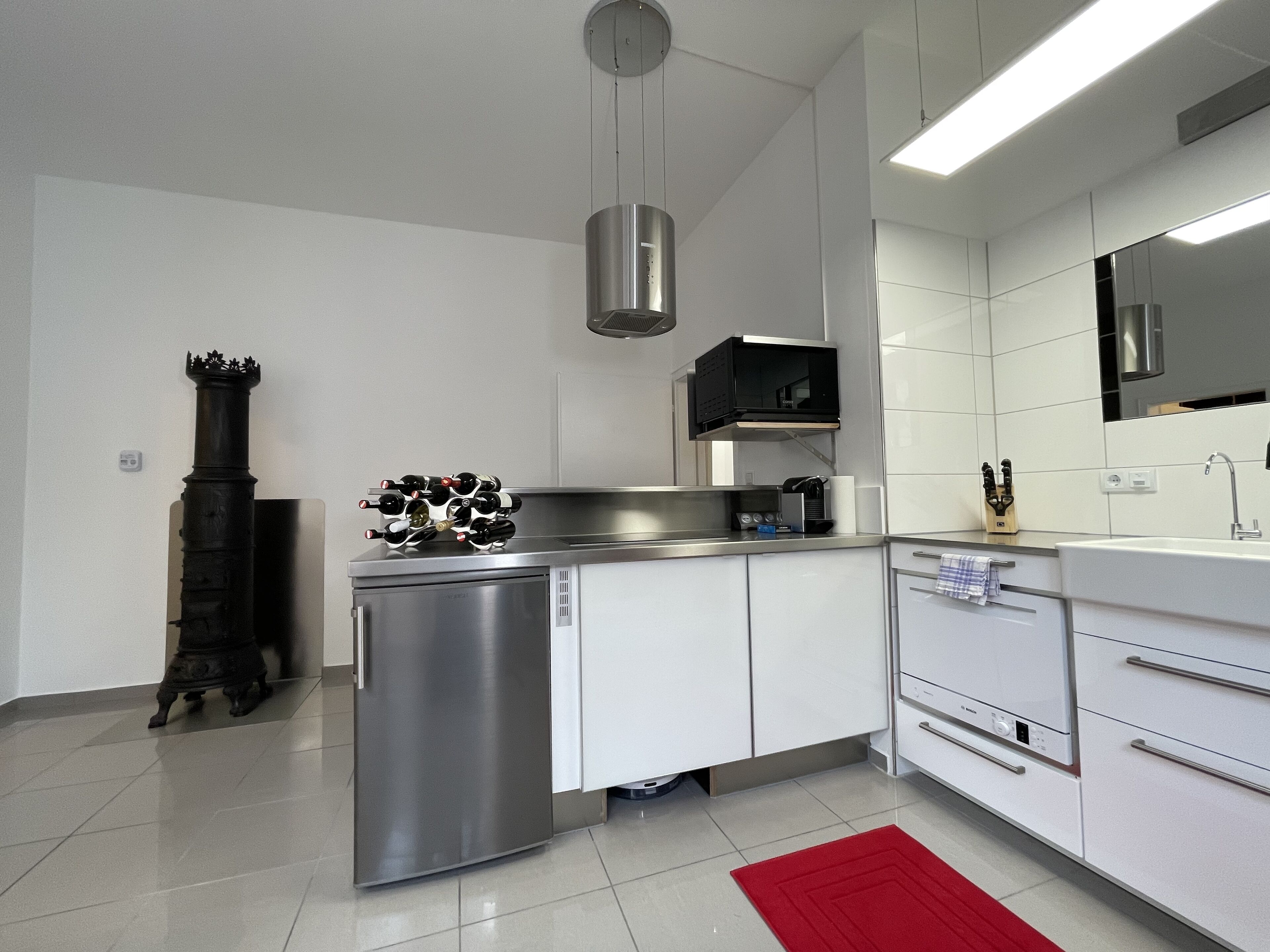 A modern kitchen with stainless steel appliances, white cabinetry, and a red rug.