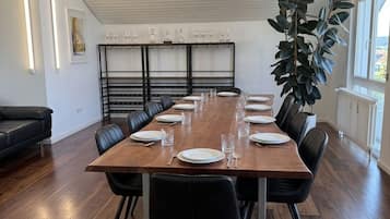 A dining room with a long wooden table, black chairs, a chandelier, and a large plant.