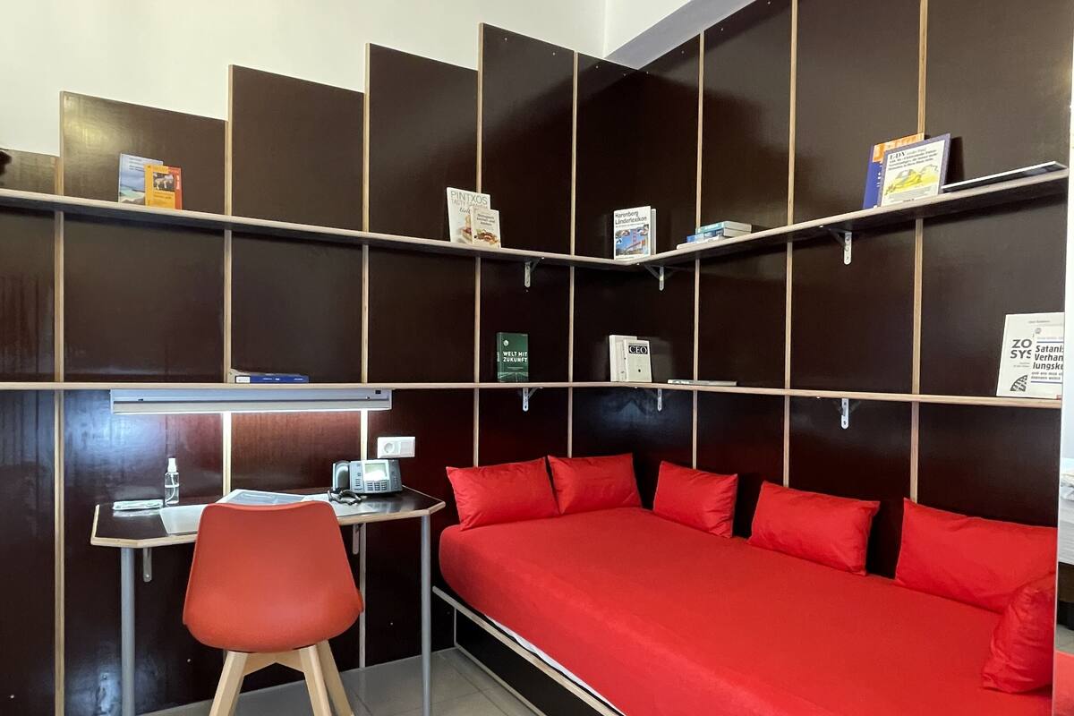 Una habitación moderna con un sofá rojo, un escritorio con una silla y estanterías llenas de libros.