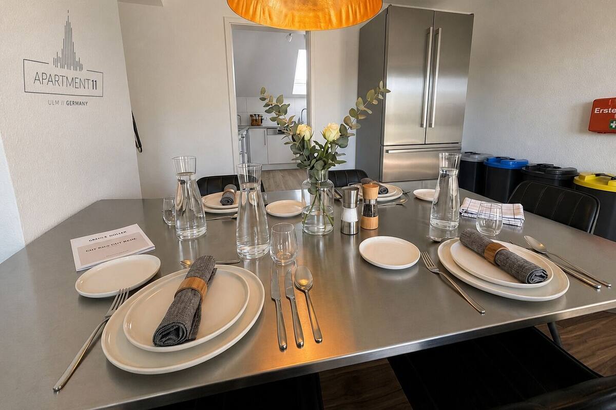 Una mesa de comedor con platos, vasos, cubiertos y un jarrón con flores.
